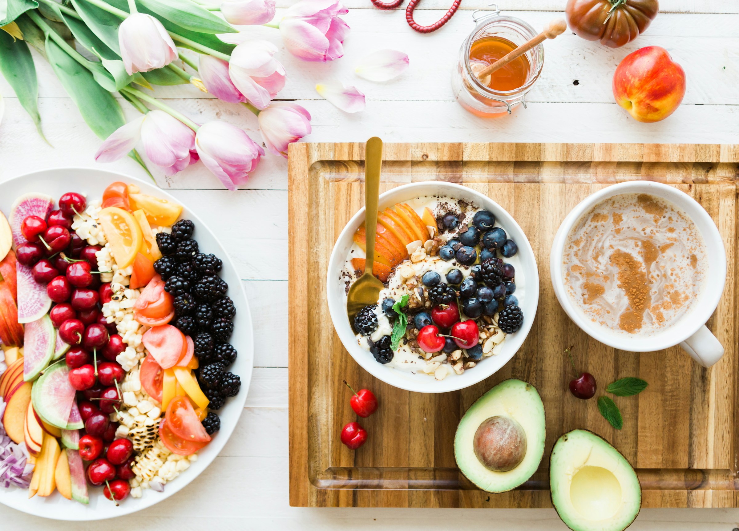Uma mesa com fruta, uma taça de iogurte e uma chávena, fotografada de cima