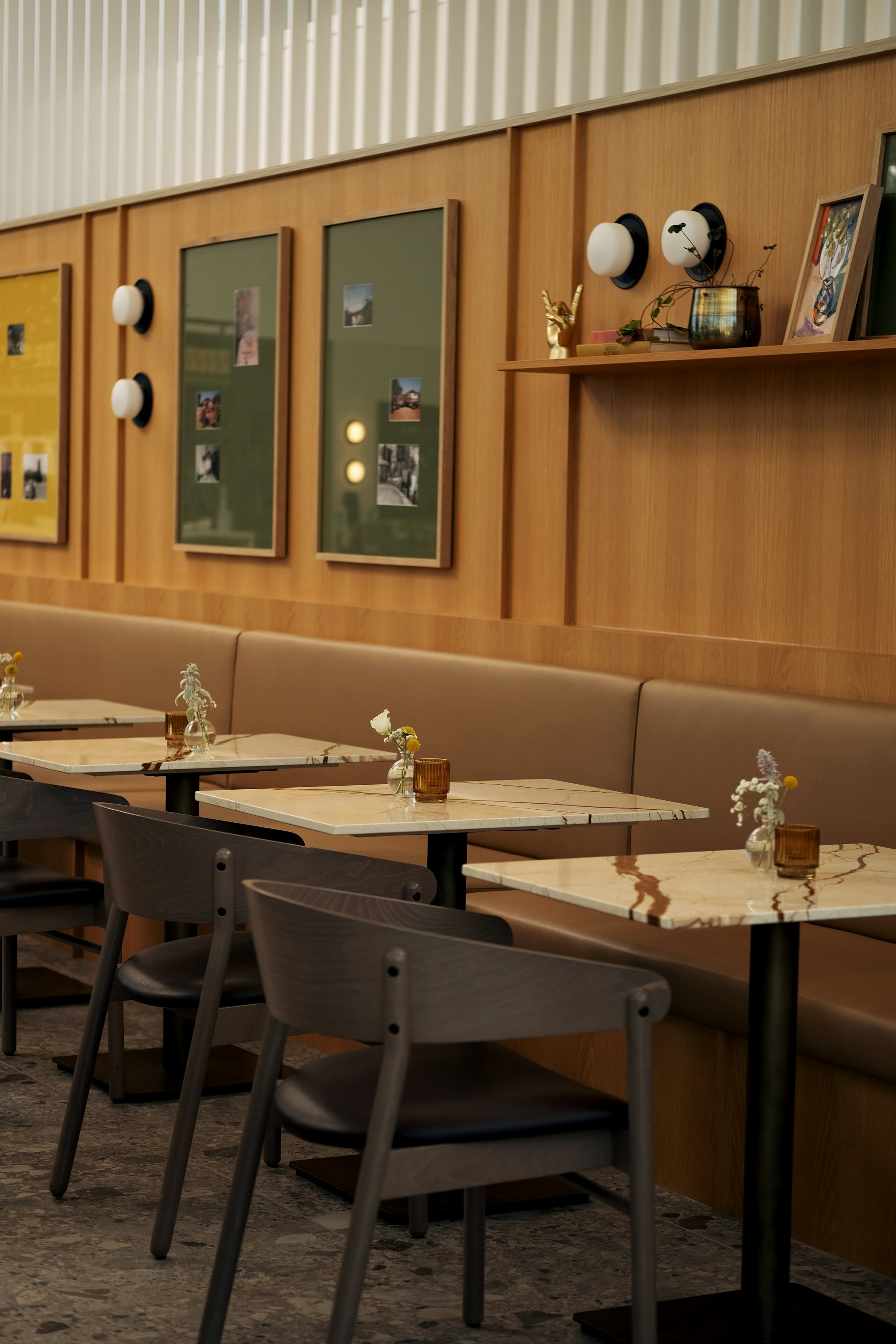 Mesas de mármore, cadeiras escuras e banco corrido num interior de restaurante com painéis de madeira e luz suave.