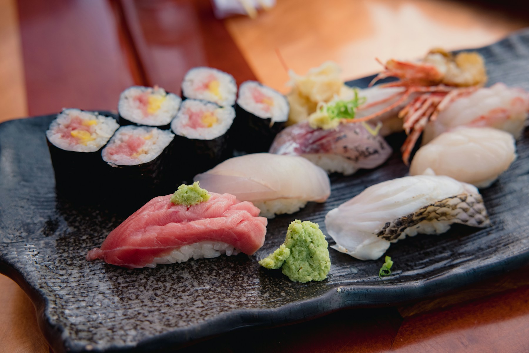 Seleção de sushi num prato de cerâmica preto, com maki, nigiri e wasabi.